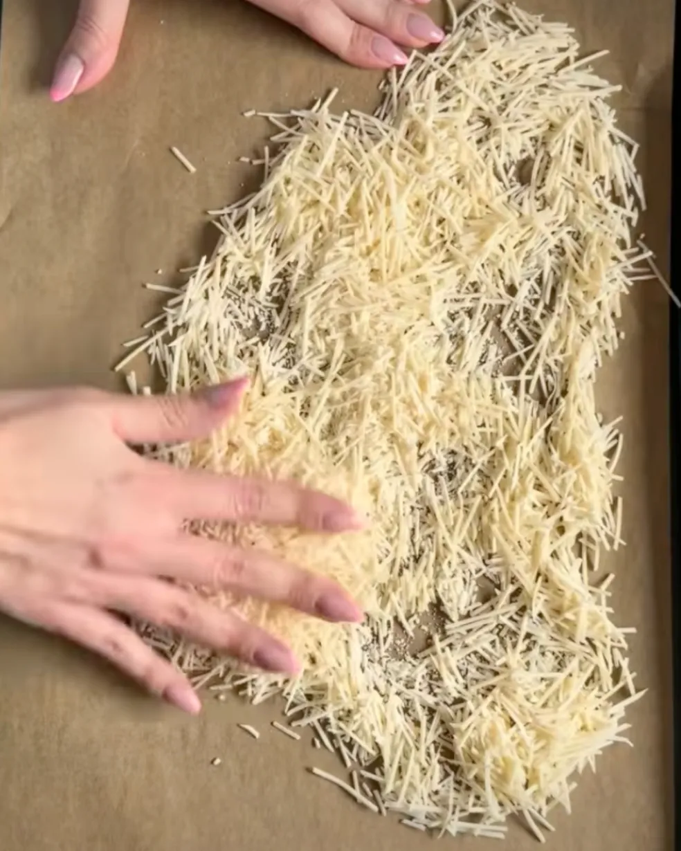 Nastrouhaný parmezán rozprostřený na papíře na pečení před vložením do trouby