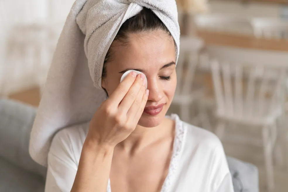 Žena si jemně odličuje oční make-up vatovým tamponkem