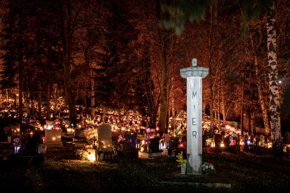 Noční hřbitov osvětlený množstvím svíček a kahanců mezi hroby